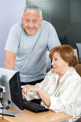 Happy Senior Man With Woman Using Computer In Classroom