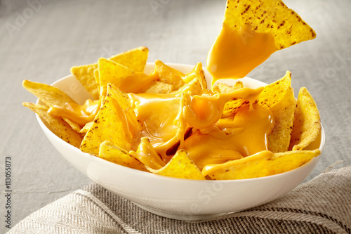Chip pulled out of bowl of cheese covered nachos photo
