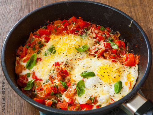 fried eggs with vegetables and cheese in a frying pan on wooden table
