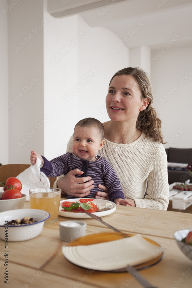 Smiling mother and baby girl looking away while sitting at table Smiling mother and baby girl looking away while sitting at table