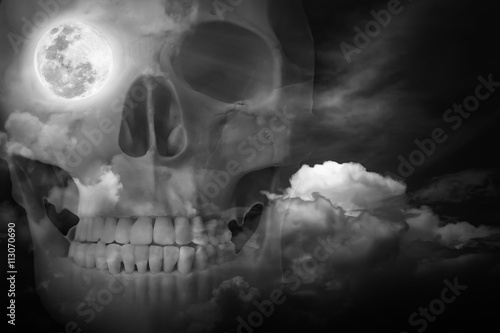 Halloween horror background. Double exposure of human skull combined sky with clouds.