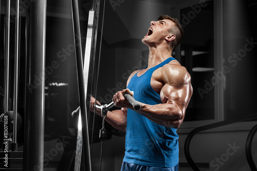 Muscular man working out in gym doing exercises at biceps, strong male