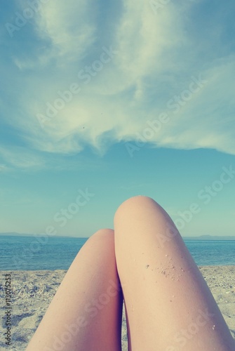 Knees of a young woman lying on the beach, on a sunny summer day, with blue sky in the background. Filtered image in faded, retro, Instagram style. Personal pov.