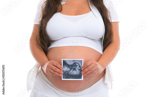 Pregnant woman holding ultrasound scan photo in front of her belly. Isolated on white background.