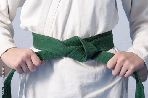Hands tightening green belt on a teenage dressed in kimono for martial arts