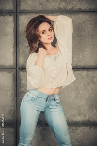 Beautiful brunette girl in jeans posing near a concrete wall. © Flash Vector