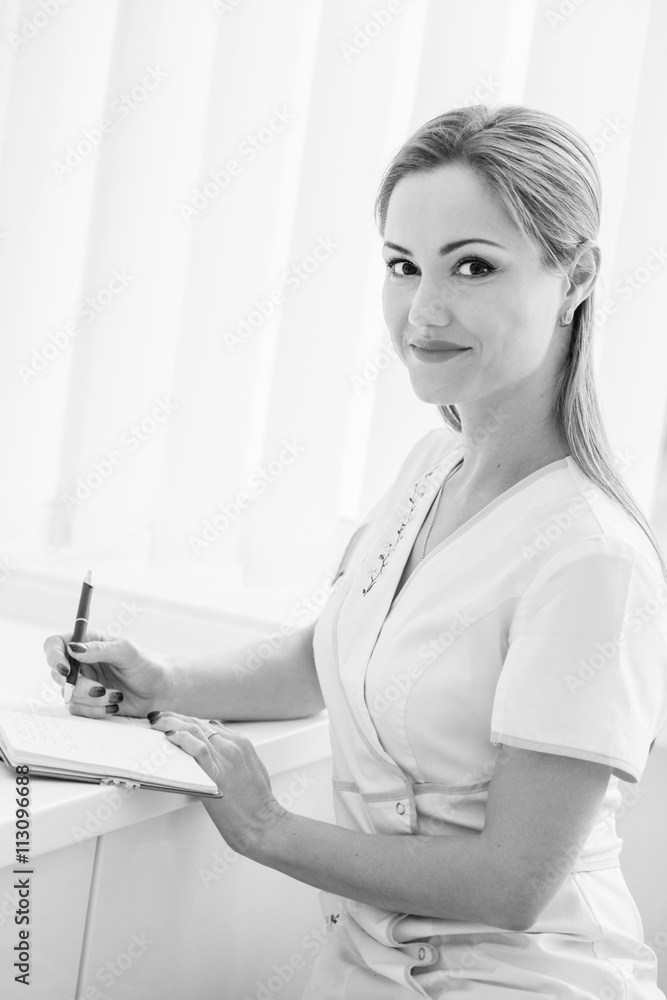 Smiling doctor sitting at desk writing Smiling doctor sitting at desk writing