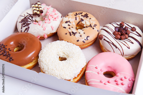 Colored delicious donuts with glaze in a box on a white wooden background