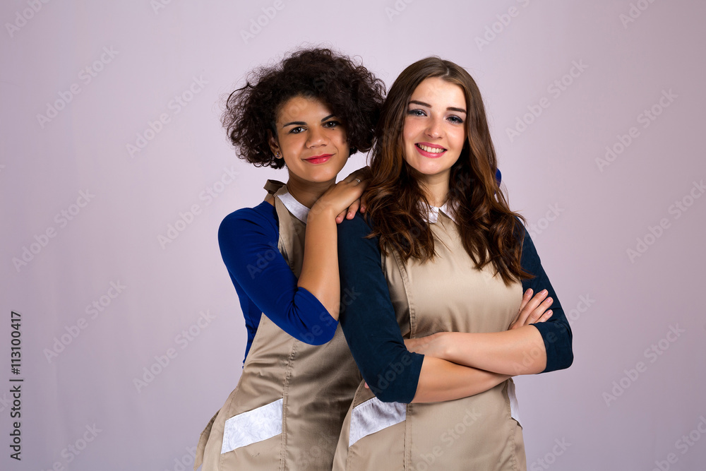 two nice girl from different nationalities Caucasian and Latina posing in studio in aprons . beauty industry two nice girl from different nationalities Caucasian and Latina posing in studio in aprons . beauty industry