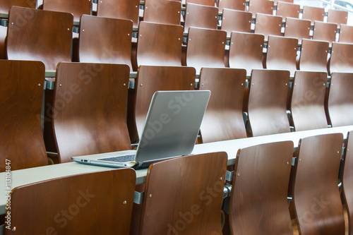 Laptop on a desk in seminar room with wooden chairs