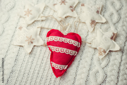 Closeup picture of handmade red heart on knitted background surrounded with decorative stars