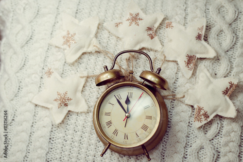 Image of alarm clock on knitted background sorounded with decorative stars photo