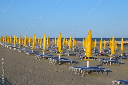 Yellow closed Sun umbrellas on sea beach with sun loungers photo