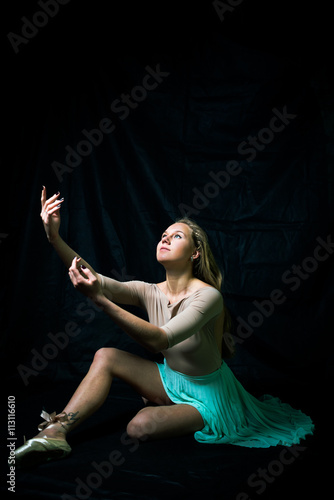 Portrait of beautiful young woman in dancing sitting on black copy space background