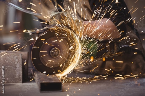 Close up of welder cutting metal with grinder in workshop
