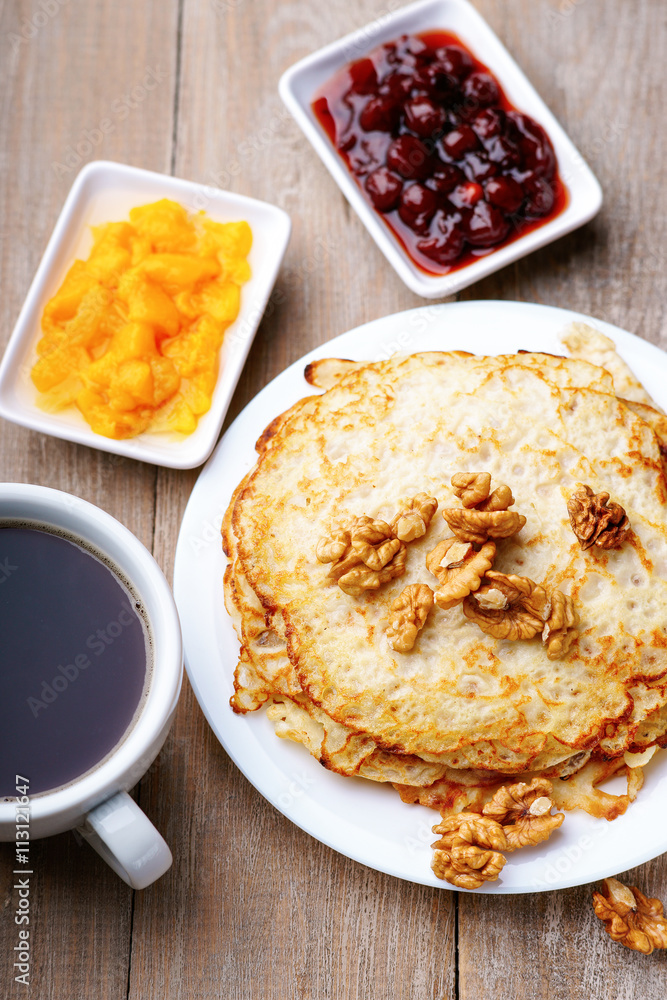 Pancakes, jam, walnuts and coffee on a wooden table