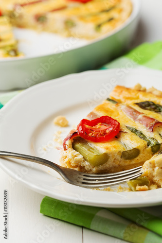 Tart with asparagus and tomatoes on white wooden background.