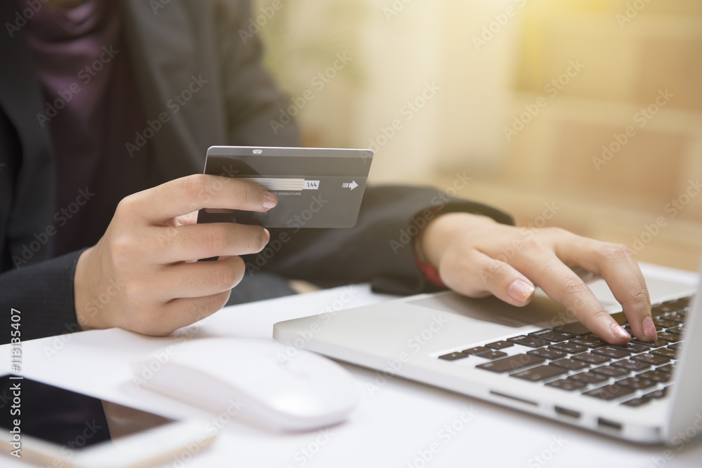 Fototapeta premium Close-up woman's hands holding a credit card and using computer