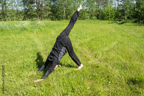 Male performs asanas on the grass.