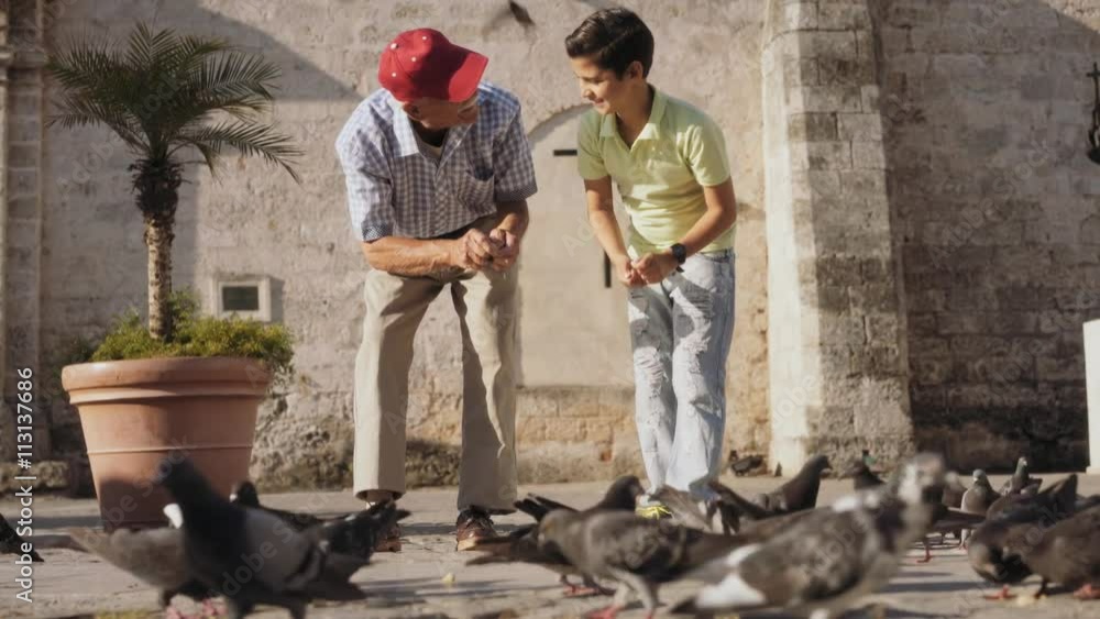 Happy tourists on holiday, during travel. Hispanic people traveling in Havana, Cuba. Grandpa and grandson feeding birds, giving food to pigeons in square. Child having fun with elderly man Happy tourists on holiday, during travel. Hispanic people traveling in Havana, Cuba. Grandpa and grandson feeding birds, giving food to pigeons in square. Child having fun with elderly man