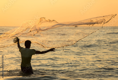 фотографія Silhouette of the unidentified Indian fisherman throwing net in sea on sunset in Fort Kochi, India