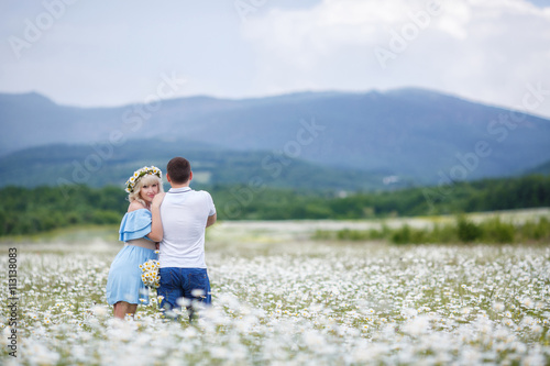 A young couple,pregnant woman,the blonde in the blue dress,man, Brunet with short hair, a shirt with short sleeves,spend time on the blossoming white flowers of the meadow