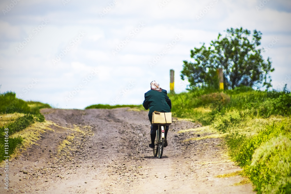 Obraz premium woman riding a bike on a country road, sky background