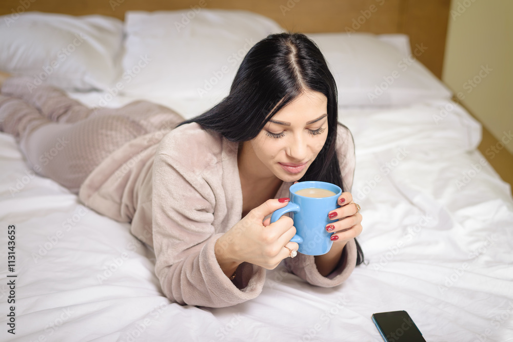 Sexy beautiful woman in bed drinking coffee tea with smartphone, portrait