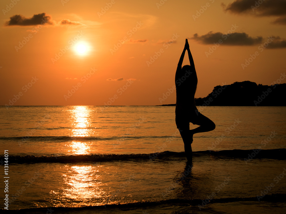 Silhouette of young woman practice yoga on sea beach at sunset in summer.