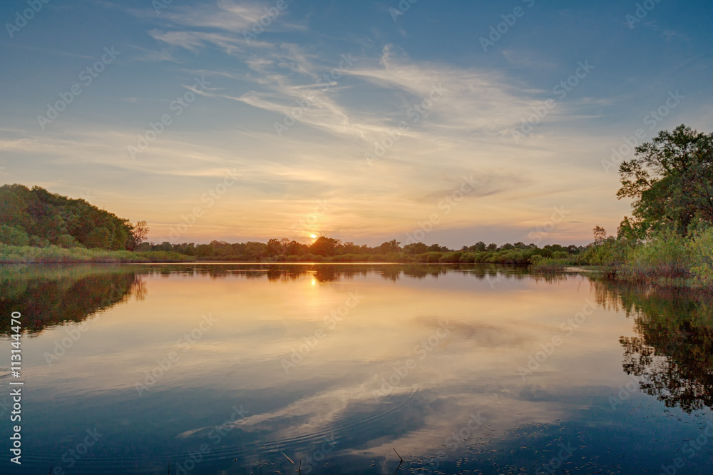Beautiful summer sunset at the river with blue sky, red and orange clouds, green trees and water