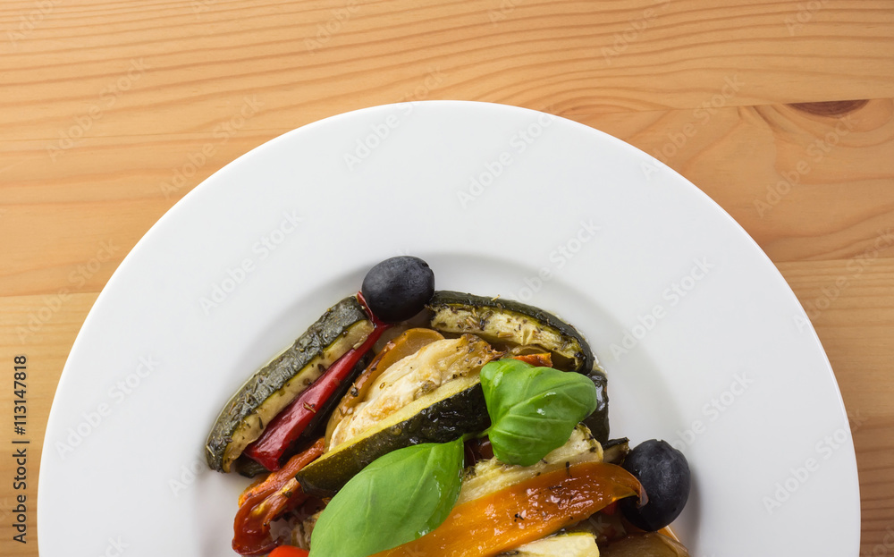Roasted vegetables on a white plate on wooden background. Top vi