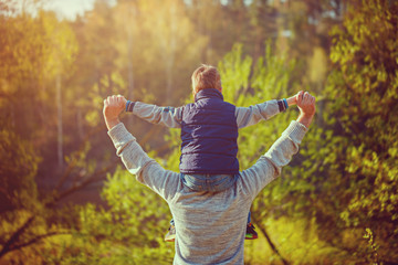 Back view of father  his son on shoulders on nature.