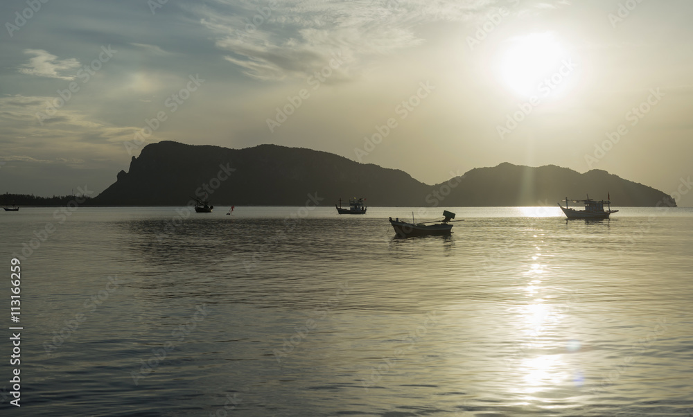 traditional boats are laying on wave surface of the sea with a long big mountain and sunrise in background.