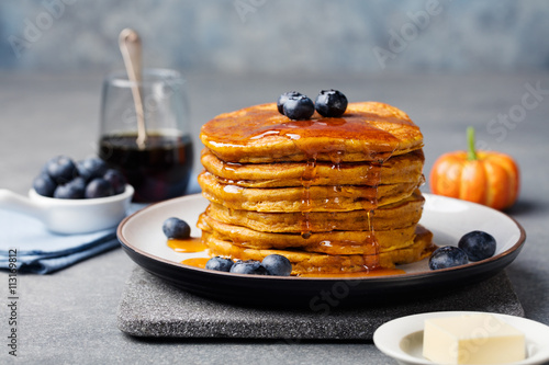 Pumpkin pancakes with maple syrup and blueberries on a plate. Grey stone background