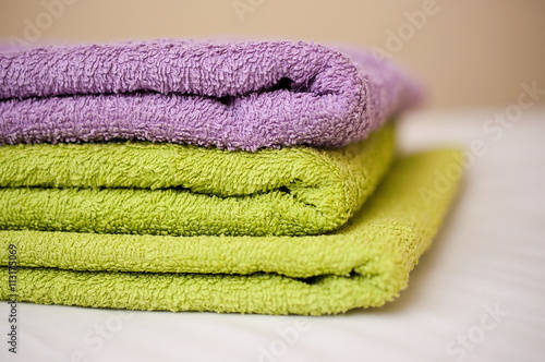 Three different colors of towels in a stack on a white bed