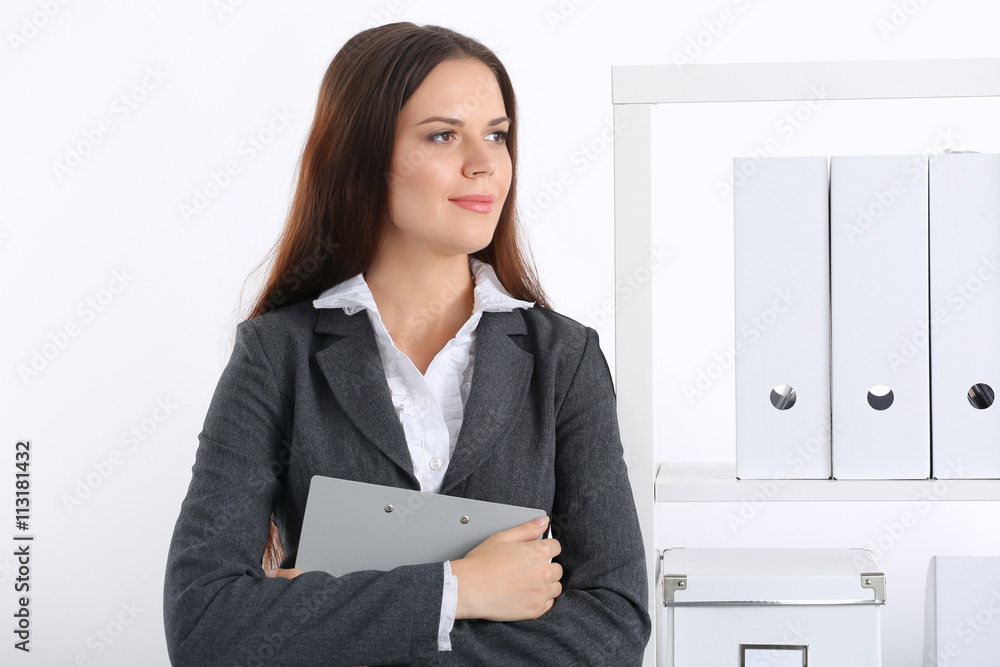 Attractive young businesswoman standing near desk with folder in the office Attractive young businesswoman standing near desk with folder in the office