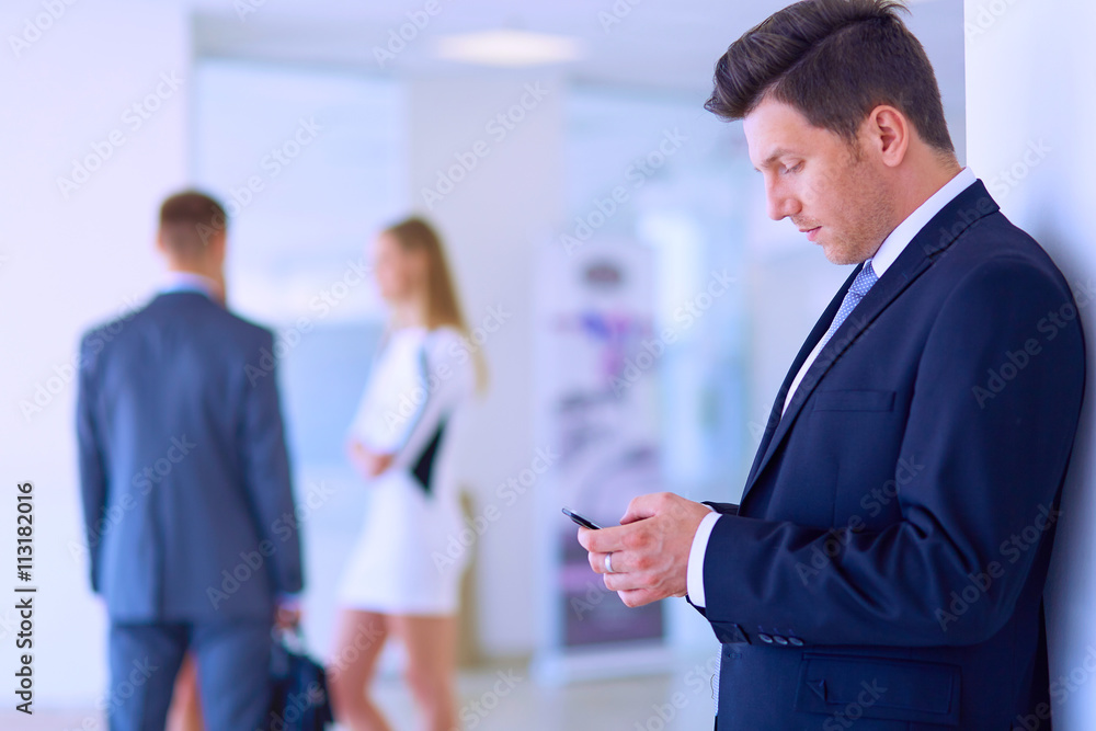 Portrait of young businessman in office with colleagues in the background and using mobile Portrait of young businessman in office with colleagues in the background and using mobile