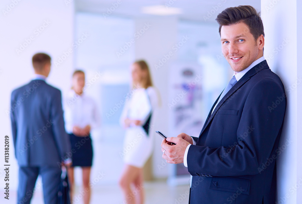 Portrait of young businessman in office with colleagues in the background and using mobile Portrait of young businessman in office with colleagues in the background and using mobile