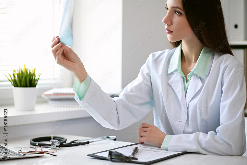 Female doctor brunette sitting at the table near the window in hospital and typing at laptop computer Female doctor brunette sitting at the table near the window in hospital and typing at laptop computer