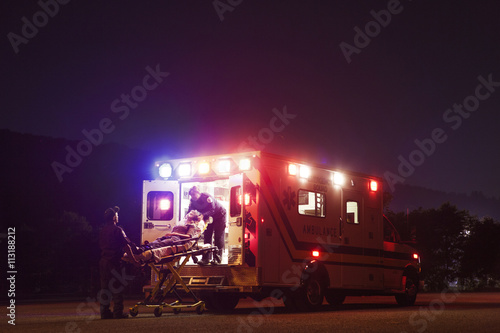 Paramedics carrying patient on stretchers into ambulance at night photo