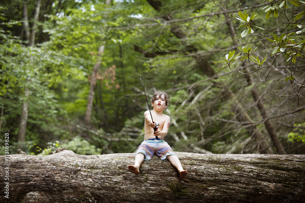 Boy (6-7) sitting on fallen tree and fishing Boy (6-7) sitting on fallen tree and fishing