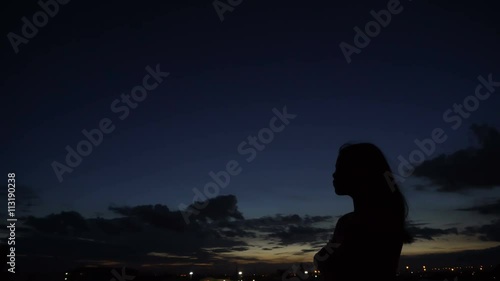 Silhouette of woman looking up at sunset sky with wind blowing hair
