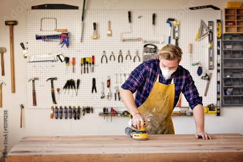 Carpenter sanding wood with sander in workshop photo