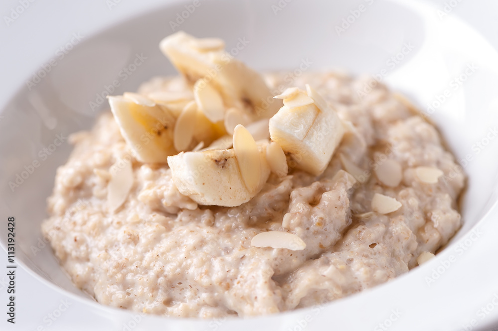 oatmeal porridge with banana  slices and almonds close-up on white plate
