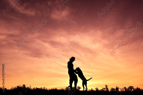 Silhouette people and dog playing at sunset