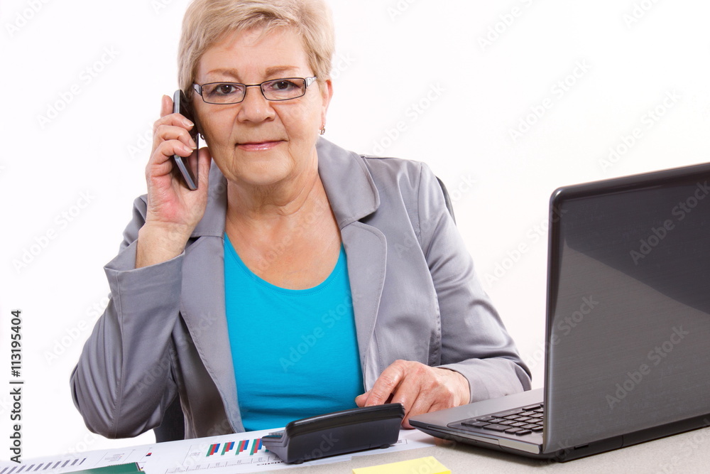 Elderly business woman talking on mobile phone and working at desk, business concept Elderly business woman talking on mobile phone and working at desk, business concept