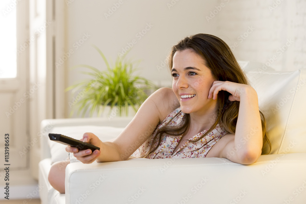young beautiful woman lying on couch holding remote control watching television happy and relaxed