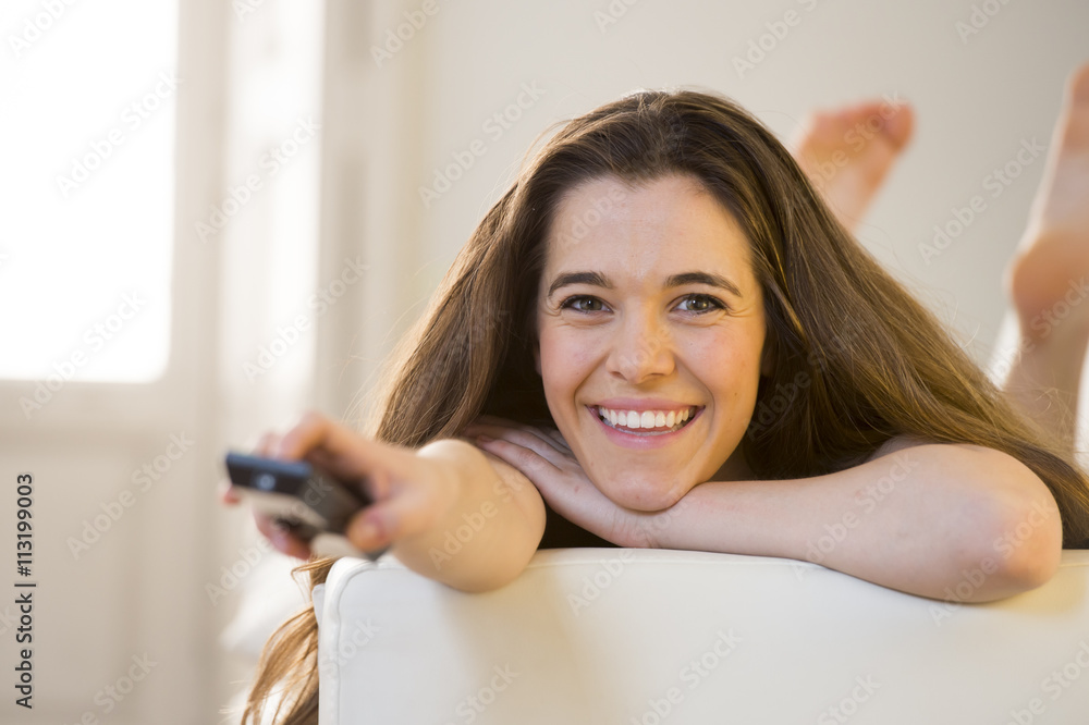 young beautiful woman lying on couch holding remote control watching television happy and relaxed young beautiful woman lying on couch holding remote control watching television happy and relaxed
