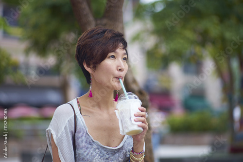 young asian woman drinking beverage in plaza