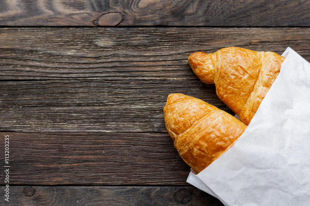 Tasty croissants in white paper bag. Rustic wooden background with sweet dessert. Top view.